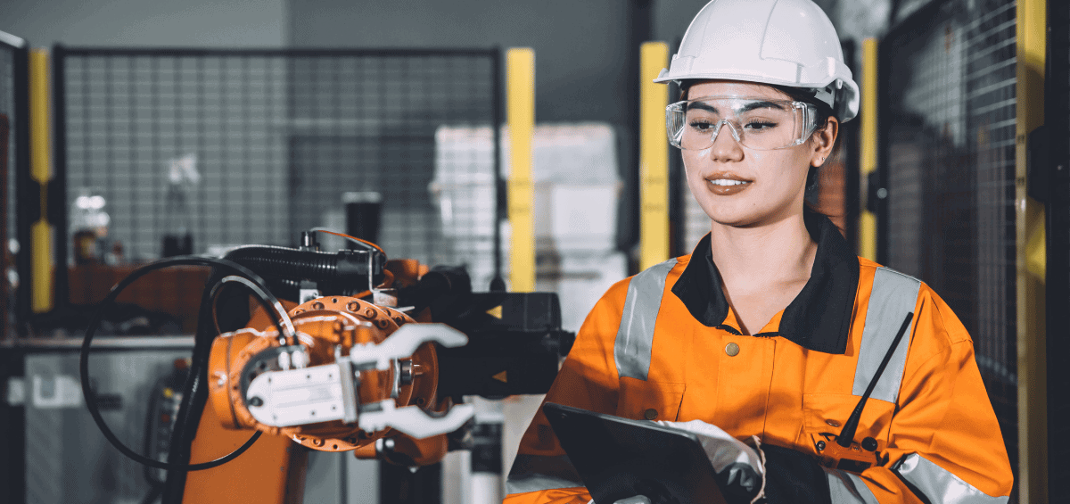 Industrial technician using a tablet to monitor and troubleshoot a robotic arm in a manufacturing facility
